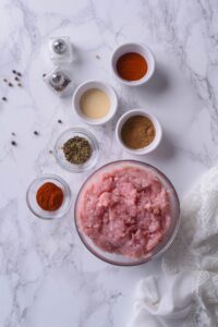 A bowl of raw ground turkey and smaller bowl of spices plus salt and pepper shakers.