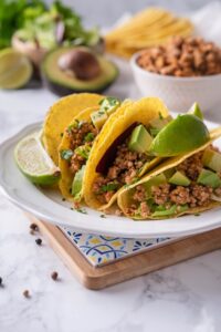 Crispy tacos stuffed with seasoned ground turkey, avocados, and cilantro on a plate with lime wedges.