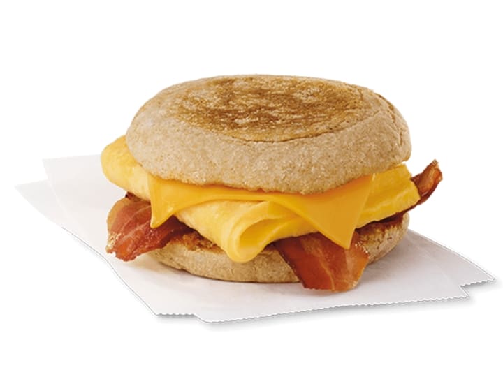 An english muffin with cheese, a folded egg, and bacon on it.