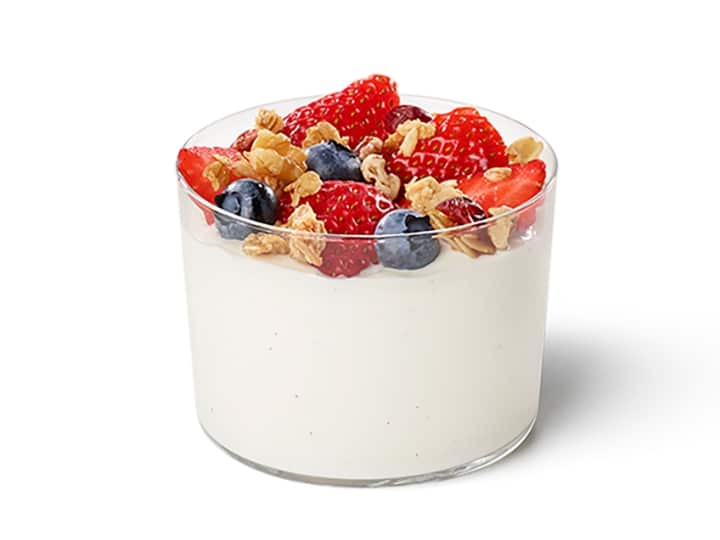 A glass cup filled with yogurt with strawberries, blueberries, and granola on top.