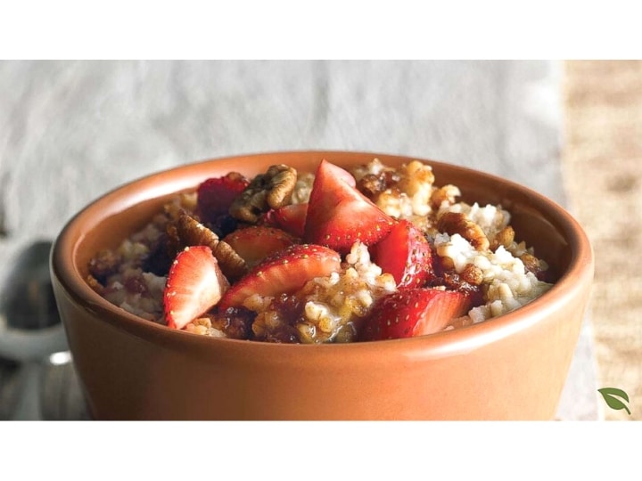 Strawberries and pecans on top of oatmeal in a brown cup.