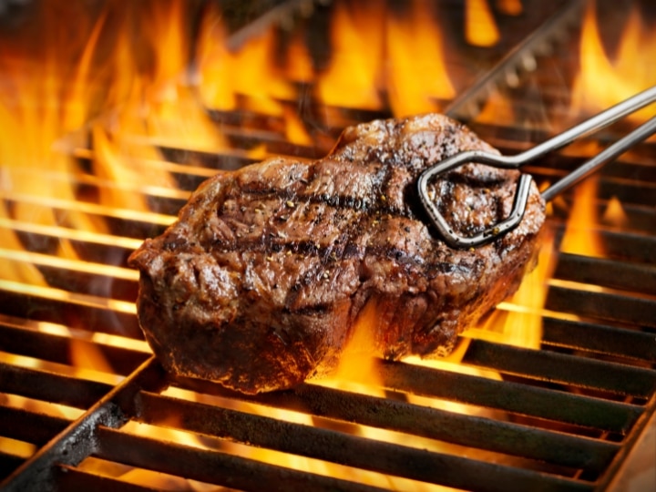 Sirloin steak being taken off a grill with tongs.