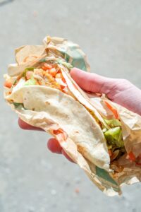 A hand holding a taco bell chicken taco with lettuce and tomatoes.