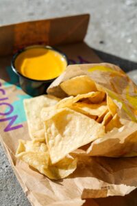 A bag of tortilla chips with a cup of nacho cheese behind it.