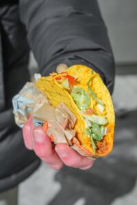 A hand holding a crunchy taco with lettuce and cheese