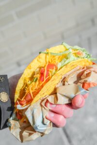 A hand holding a crunchy taco with tomatoes, lettuce and cheese.