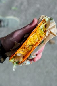 A hand holding a Doritos locos taco with shredded lettuce and cheese.