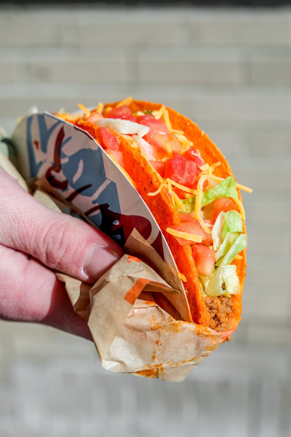 a hand holding a taco bell doritos locos taco with lettuce, tomatoes, and cheese.