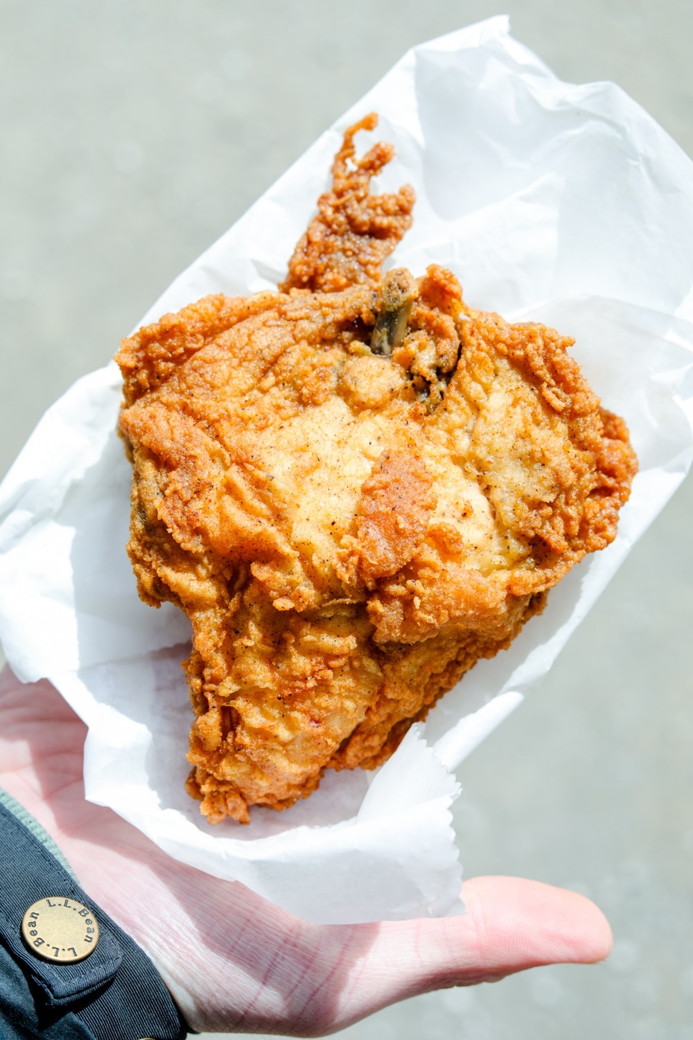 A hand with an open palm holding a KFC original recipe chicken breast.