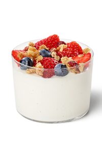 A glass cup with yogurt in it with berries and granola on top.