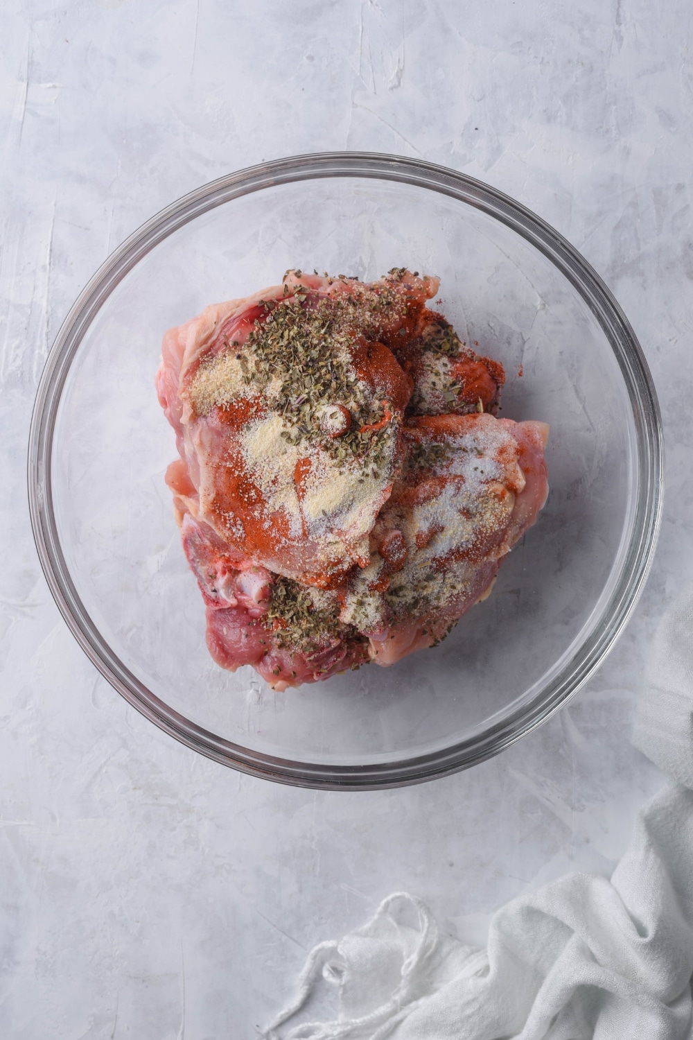 Raw chicken thighs with seasoning in a glass bowl.