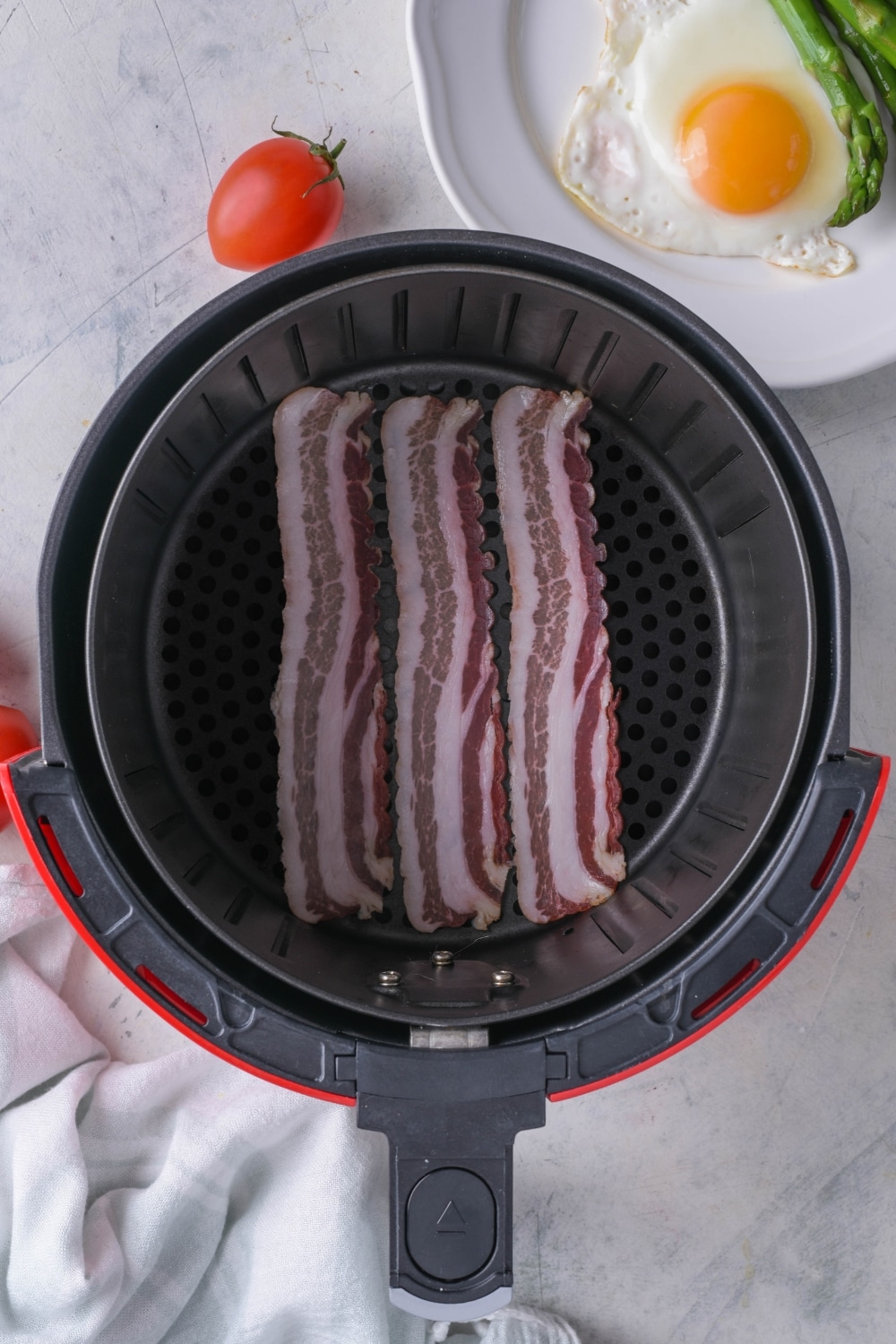 Three strips of uncooked thin cut bacon arranged in an air fryer basket.