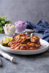 A couple of BBQ grilled chicken thighs on a white plate.