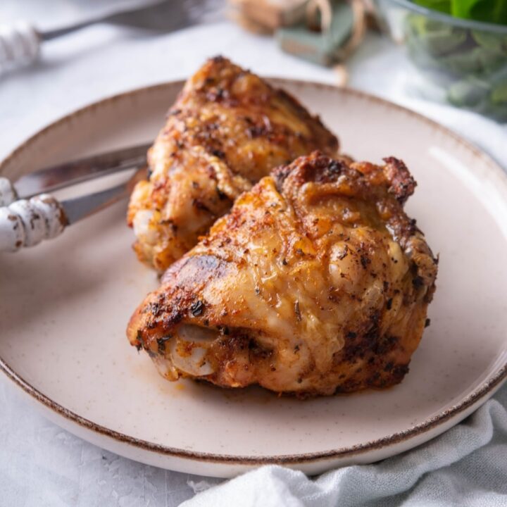 Close up of air fryer chicken thighs on a plate with a knife and fork.