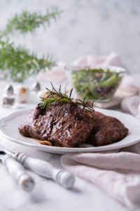 Two sirloin steaks that are against one another on a white plate.