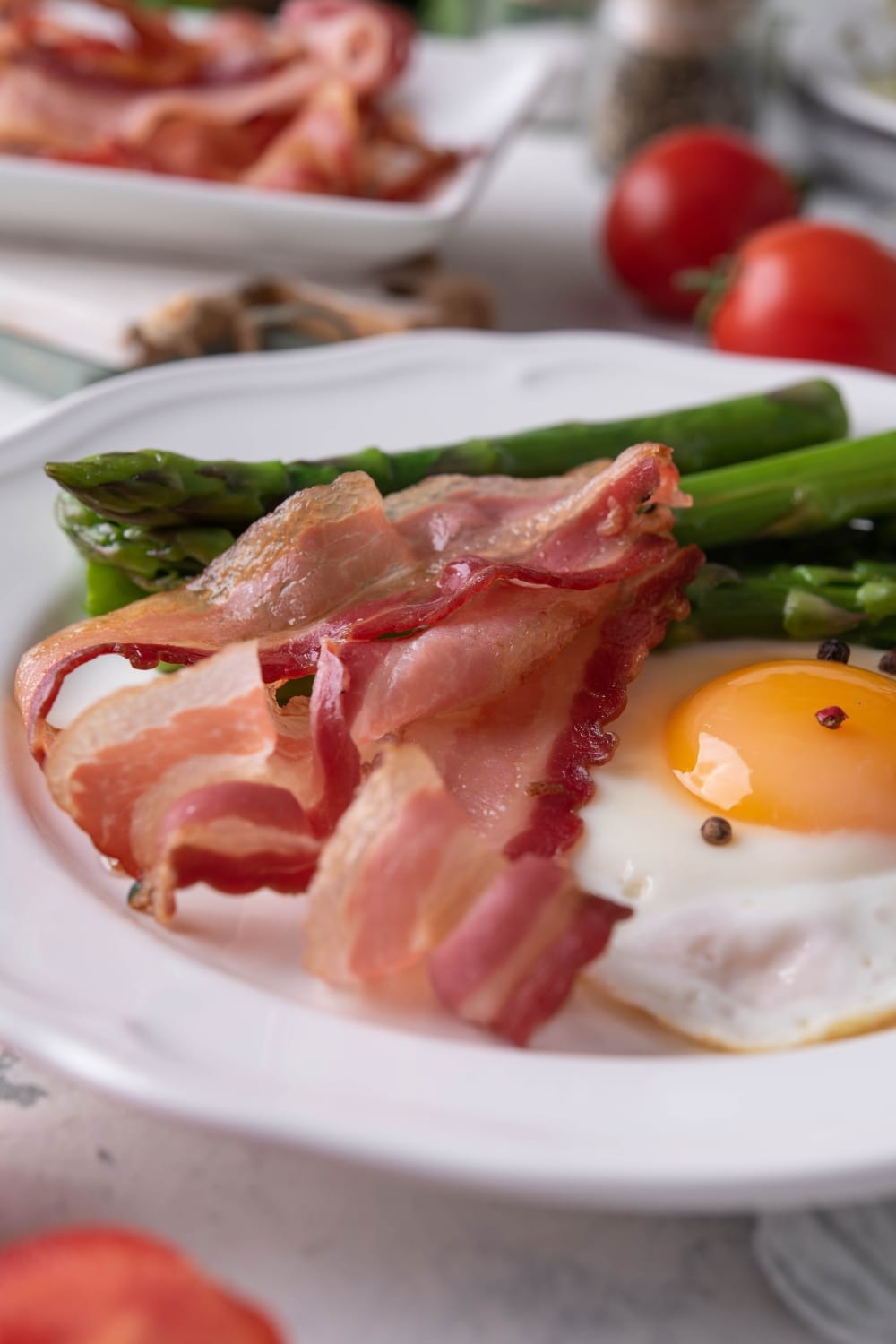 Close up of air fried bacon strips on a plate with a sunny side up egg and cooked asparagus.