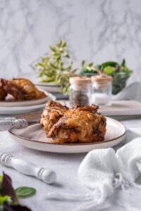 Air fryer chicken thighs on a plate with a knife and fork. Behind is a plate with more air fried chicken thighs and a pair of salt and pepper shakers.