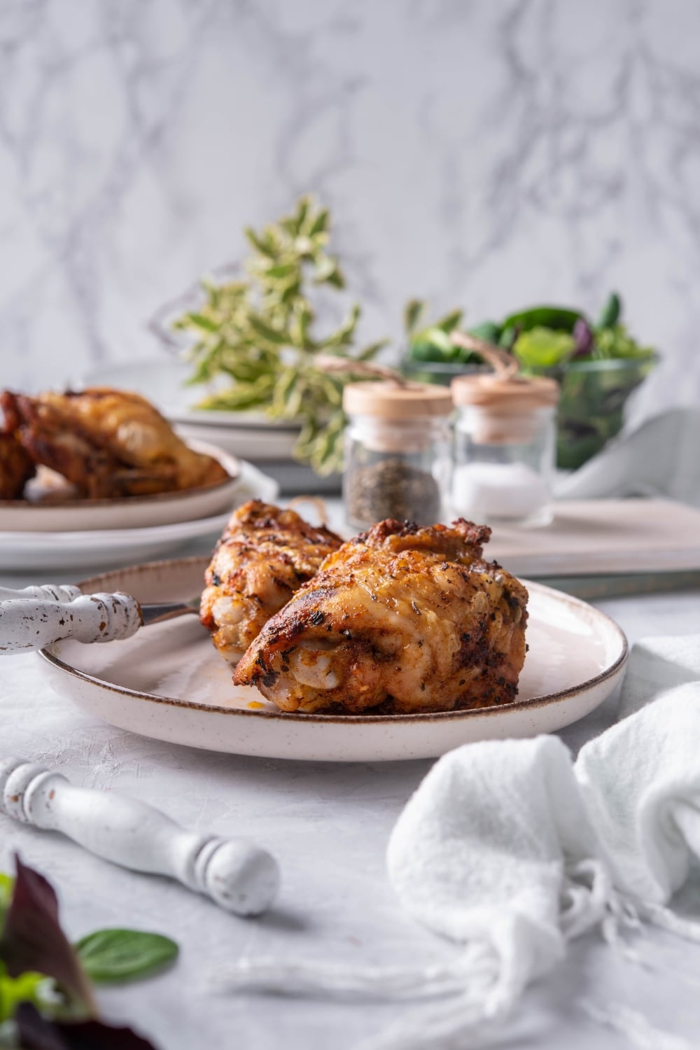 Air fryer chicken thighs on a plate with a knife and fork. Behind is a plate with more air fried chicken thighs and a pair of salt and pepper shakers.