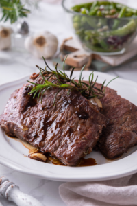 A sirloin steak leaning against another steak on a white plate.