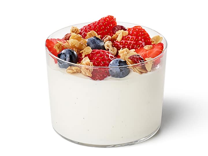 Berries and granola on top of yogurt in a glass bowl.