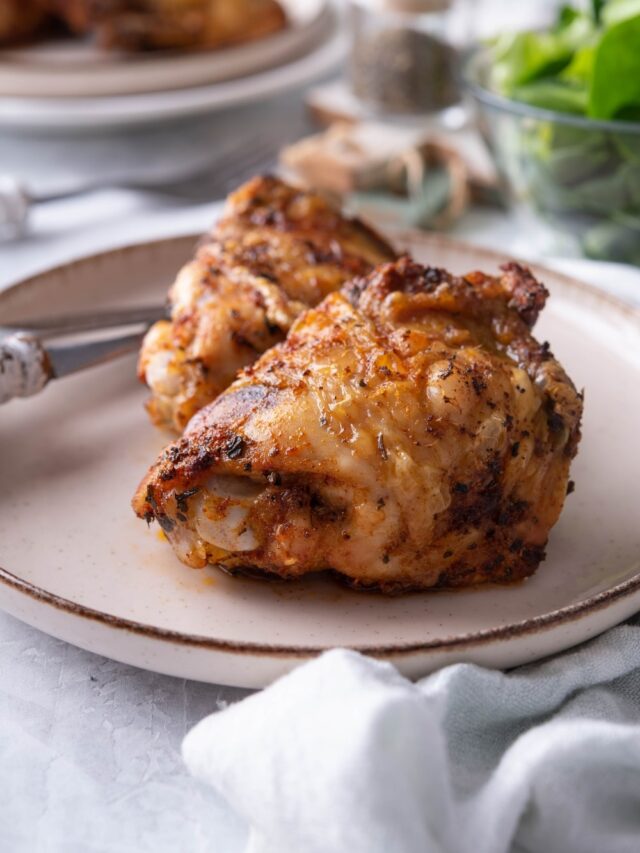 Seasoned air fried chicken thighs on a plate with a knife and fork.