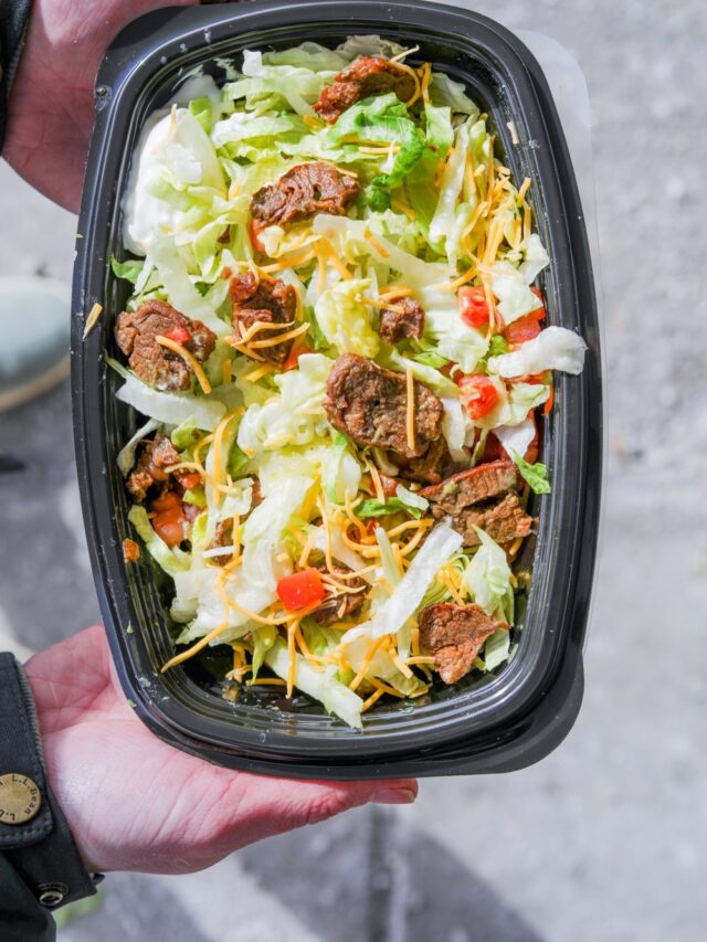 A hand holding a taco bell veggie power bowl with lettuce, steak, cheese, and tomatoes.