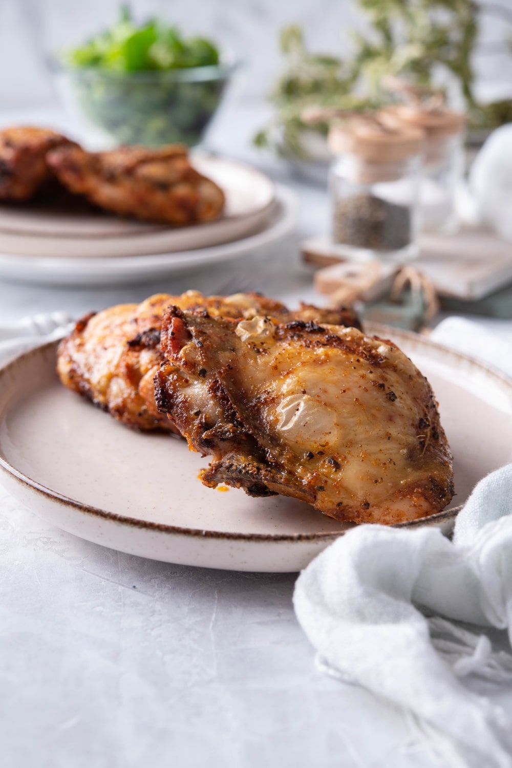 Crispy air fried chicken thighs on a plate. Behind is a plate with more air fried chicken thighs and a pair of salt and pepper shakers.