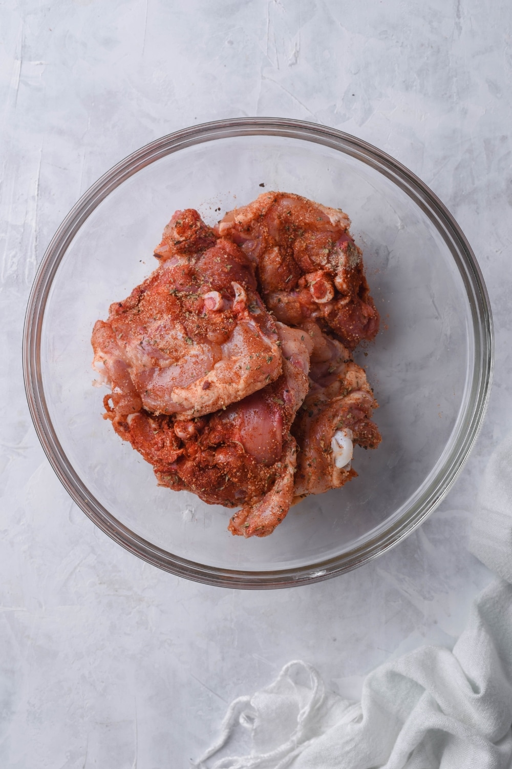 Seasoned raw chicken thighs in a glass bowl.