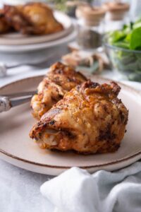 Seasoned air fried chicken thighs on a plate with a knife and fork.