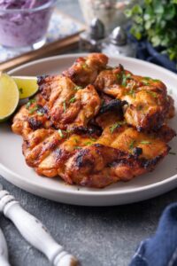 A bunch of BBQ grilled chicken thighs on top of one another on a white plate.