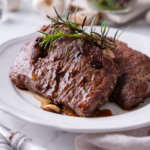 Two juicy cast iron steaks on a white plate.