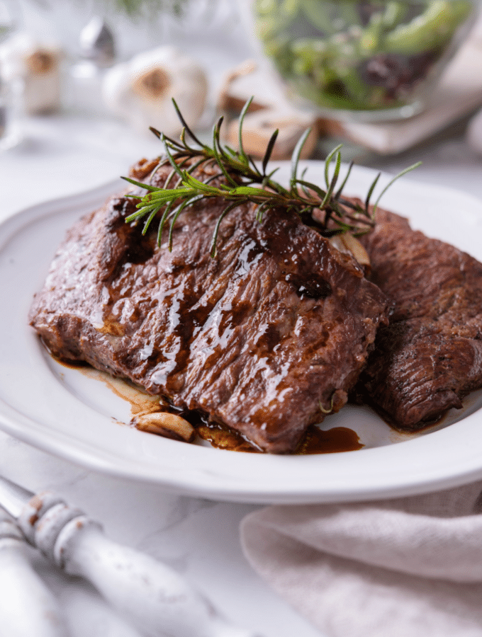 Two juicy cast iron steaks on a white plate.