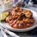 A few gilled chicken thighs that are on a white plate.