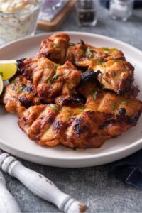 Four bbq grilled chicken thighs on a white plate.