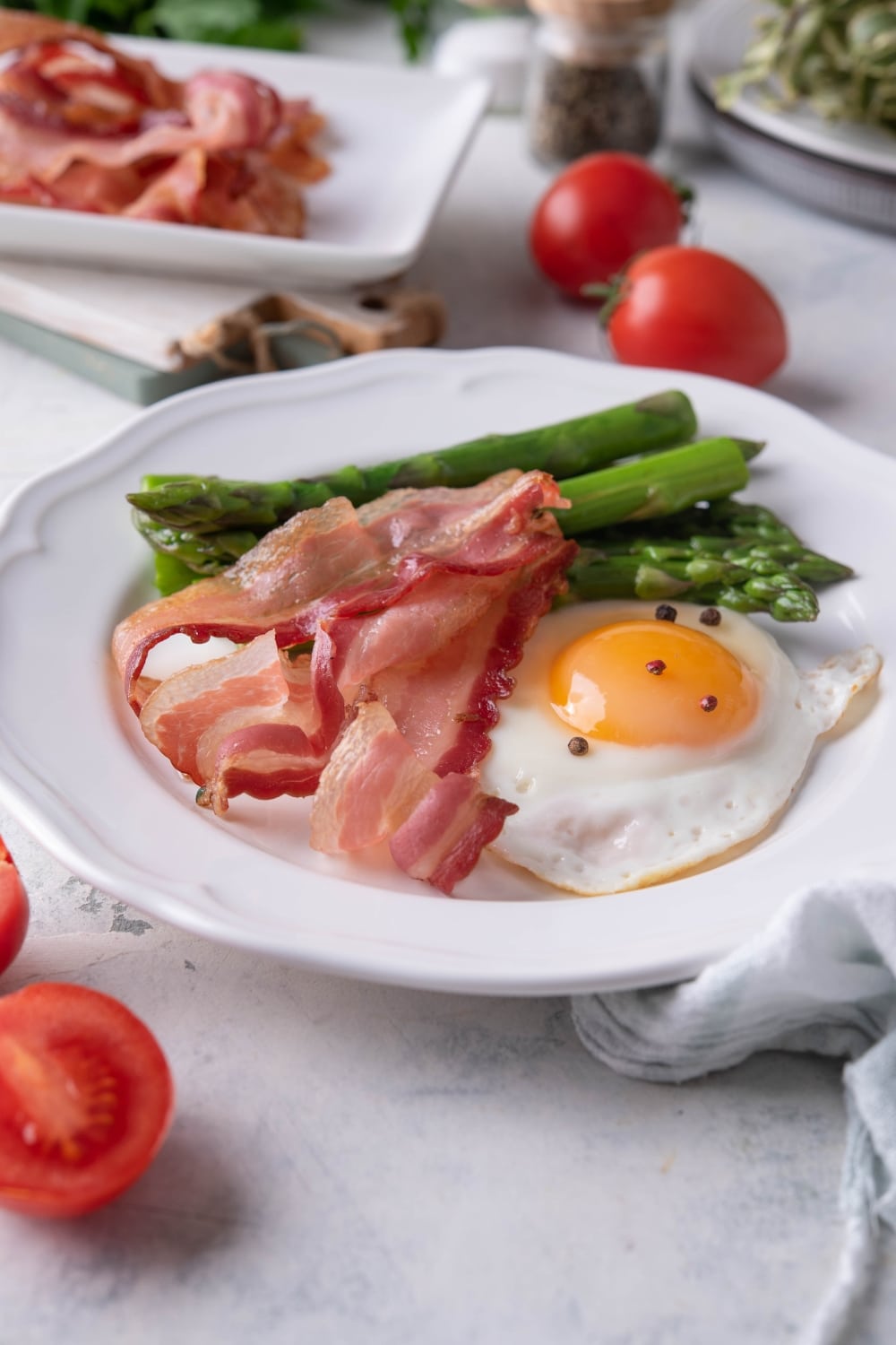 Three air fried bacon strips on a plate with a sunny side up egg and cooked asparagus.