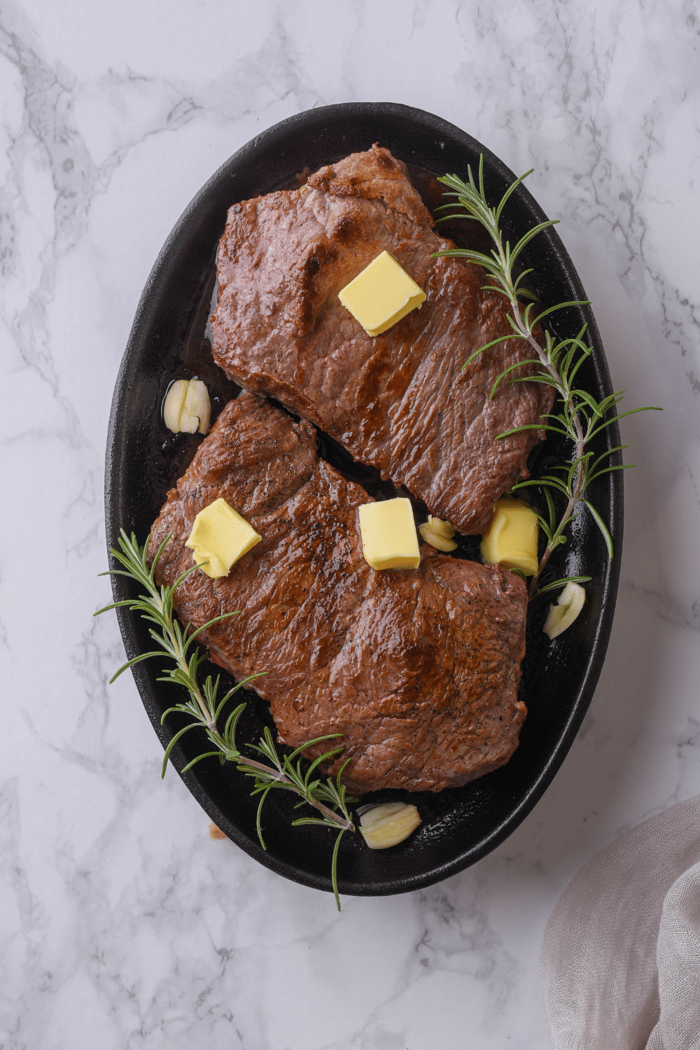 A bunch of cubes of butter on two cooked sirloin steaks in a cast iron.