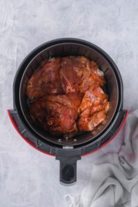 Seasoned raw chicken thighs arranged in one layer in an air fryer basket.