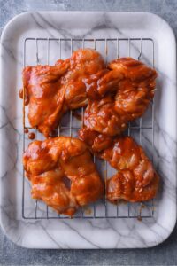 BBQ chicken thighs on top of a wire rack on a serving tray.