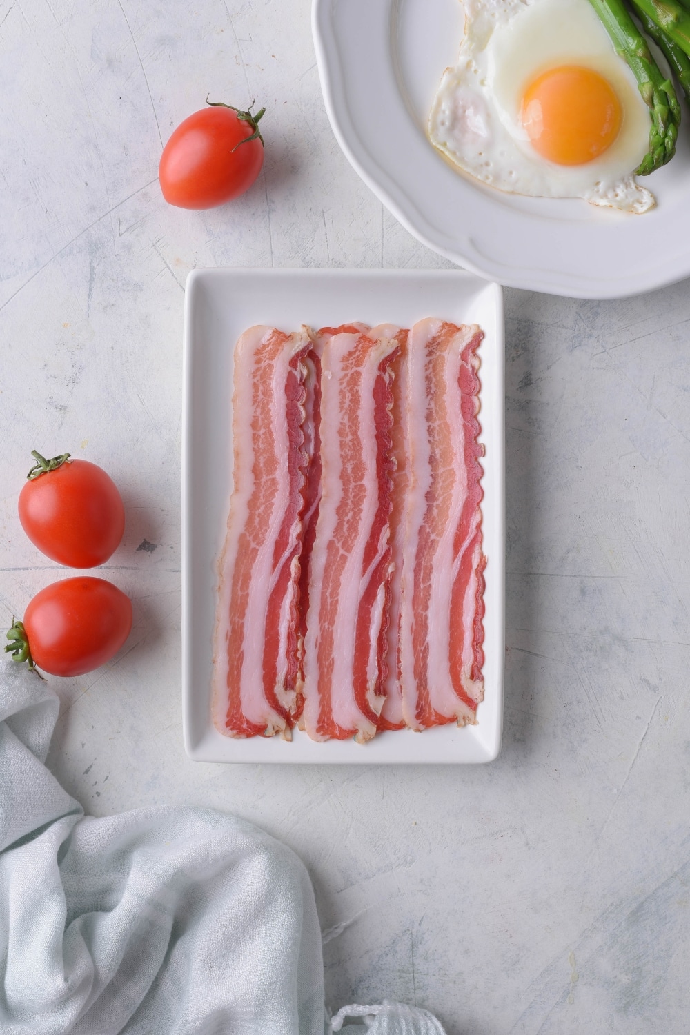 Three strips of raw bacon on a rectangle plate.