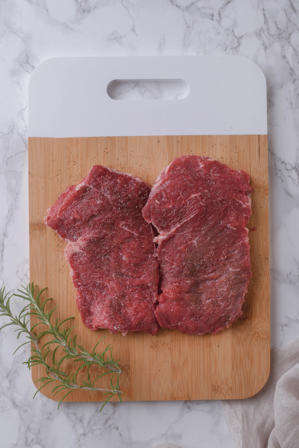 Two seasoned sirloin steaks on a cutting board.