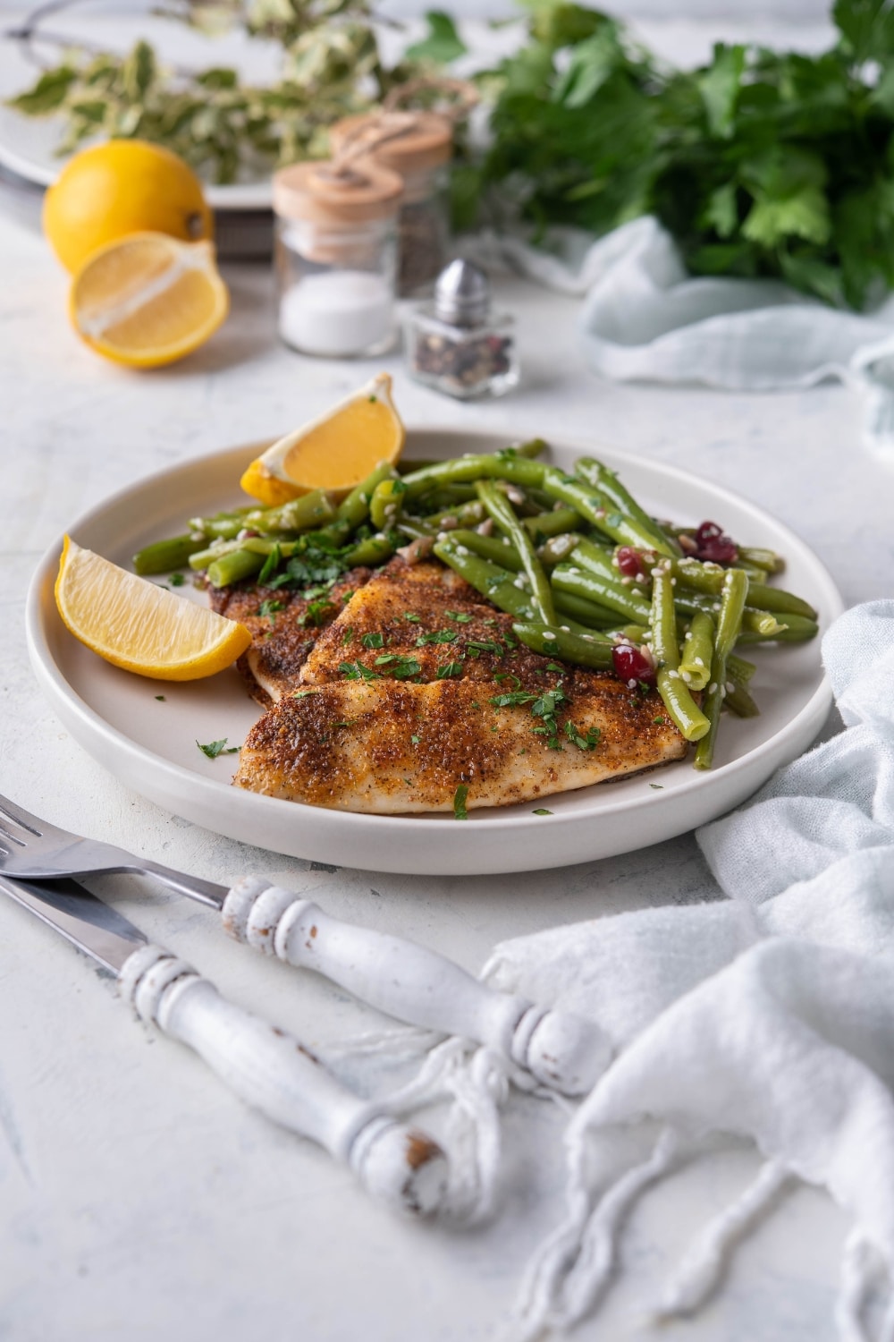 Grilled tilapia filets with sauteed green beans and lemon wedges on a white plate.