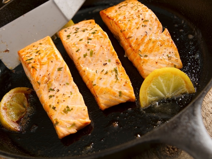 Three salmon filets in a cast iron skillet.