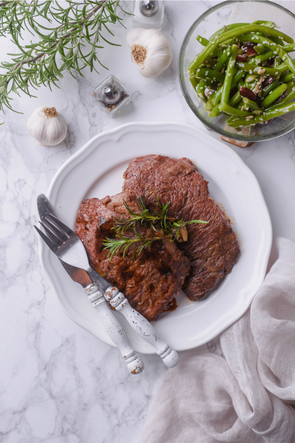 Two sirloin steaks on top of a white plate with a bowl of green beans in front of it.