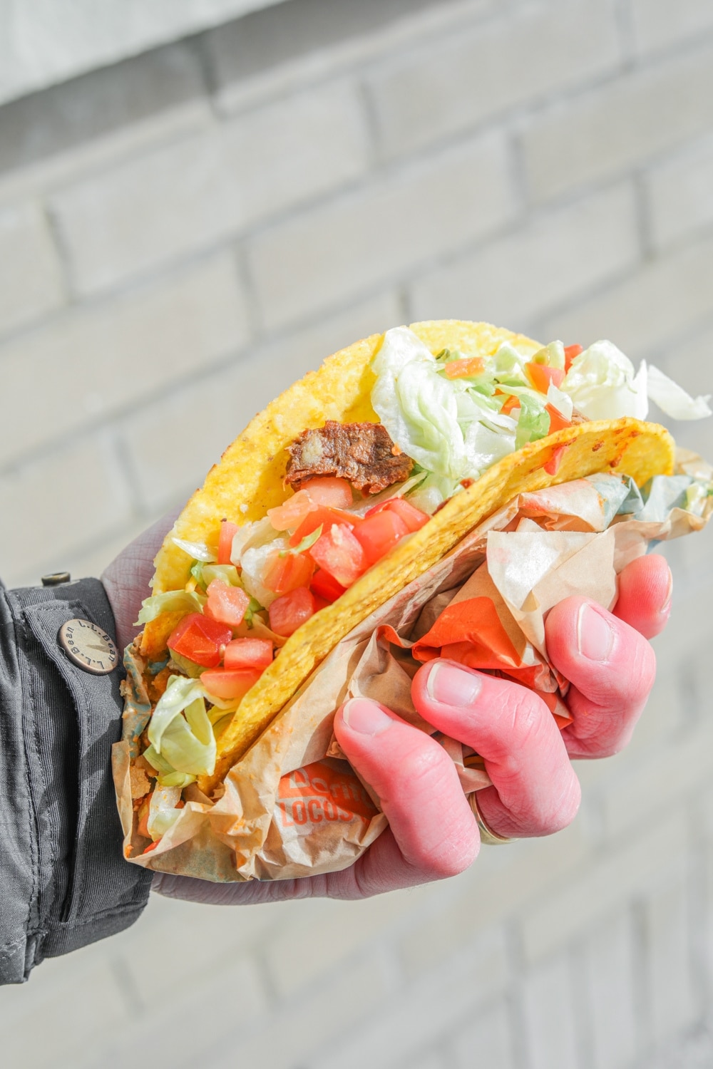 a hand holding a crunchy steak taco with lettuce and tomatoes.