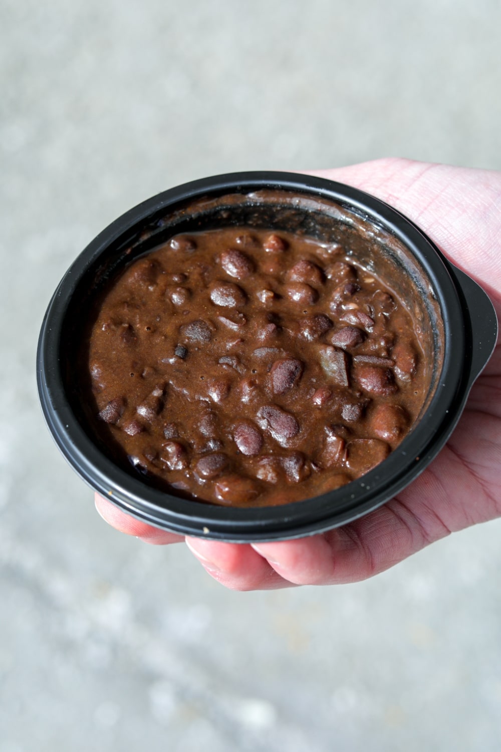 A hand holding a cup of black beans.