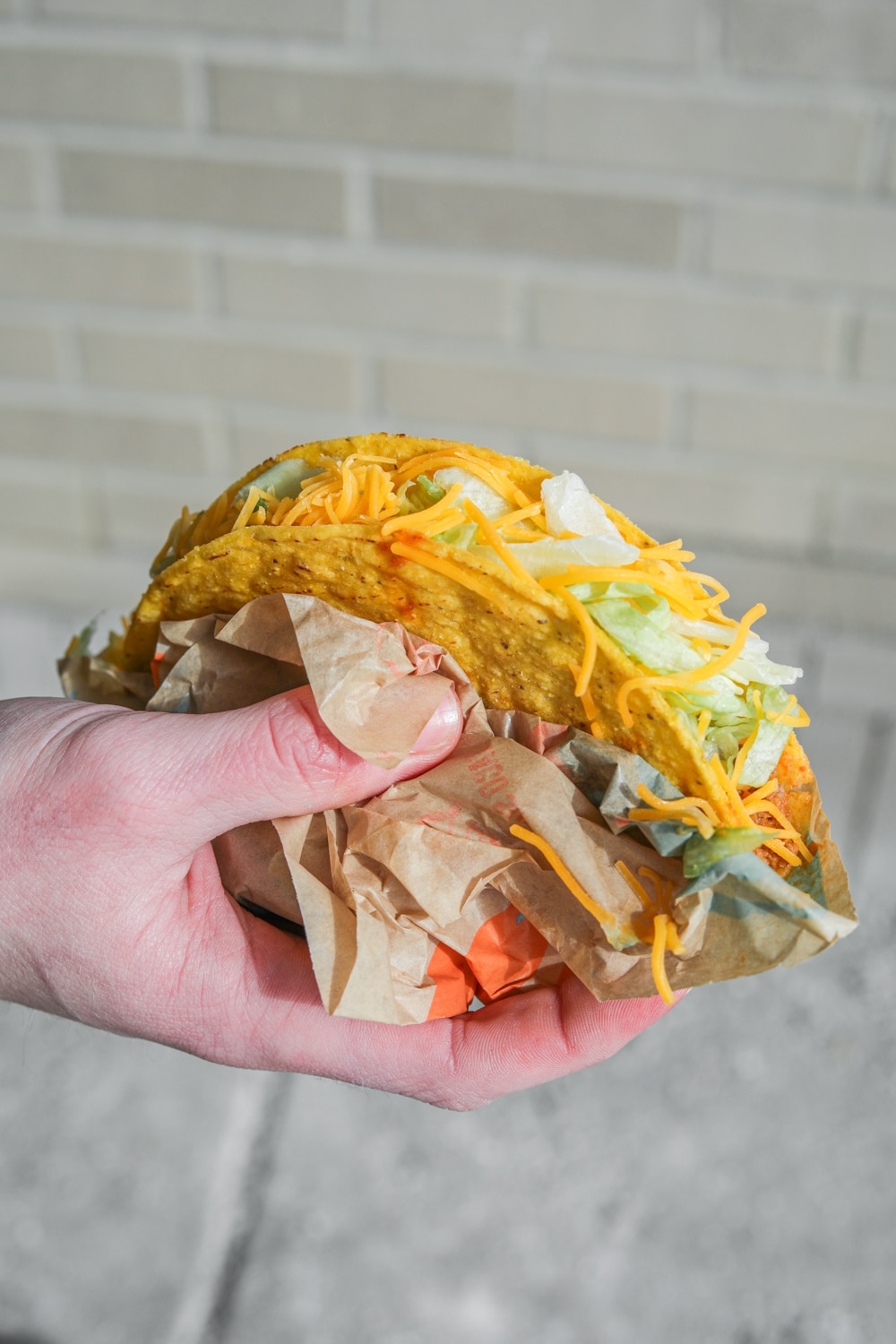 A hand holding a crunchy beef taco with lettuce and shredded cheese.