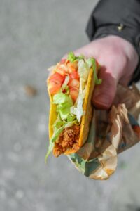 A hand holding a taco bell crunchy taco with beef, shredded lettuce, and tomatoes.