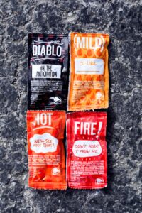 A diablo sauce packet, a mild sauce packet, a hot sauce packet, and a fire sauce packet all on in a square formation on a black surface.