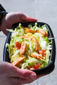 A hand holding a taco bell veggie power bowl with chicken strips on top of shredded lettuce and tomatoes.