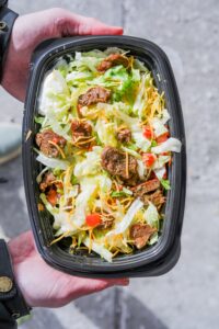 A hand holding a taco bell veggie power bowl with lettuce, steak, cheese, and tomatoes.